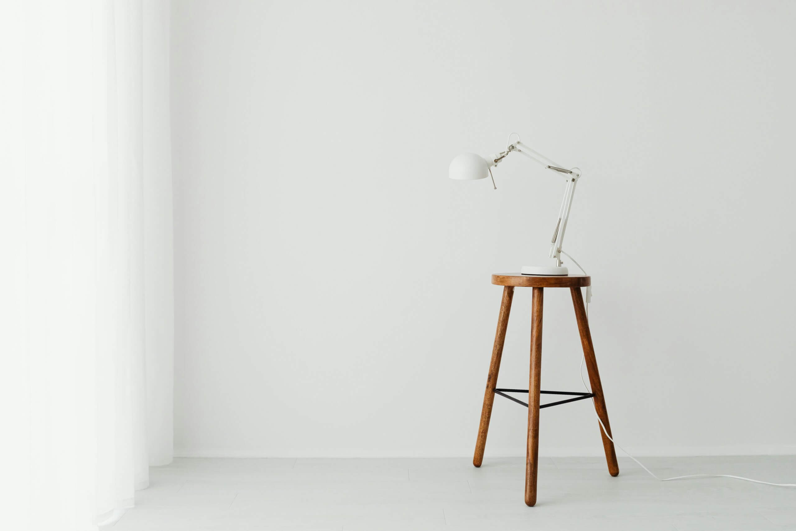 Simple minimalist setup with a white desk lamp placed on a wooden stool against a white wall.